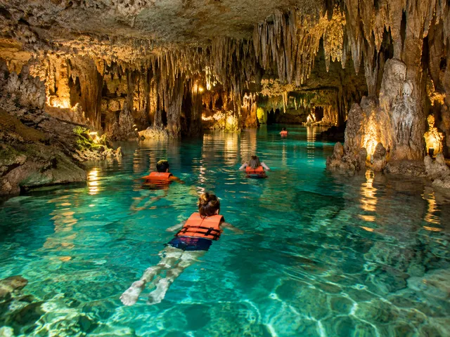 Des nageurs en gilets de sauvetage dans une rivière souterraine claire parmi les stalactites